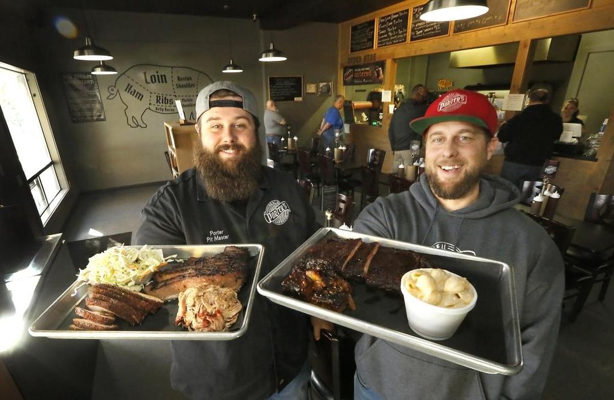 Brothers Porter Kinney, left, and Reed Kinney hold trays of the smoked meats and sides they cook for their Porter’s Real Barbecue restaurants in Richland, Pasco and Kennewick.