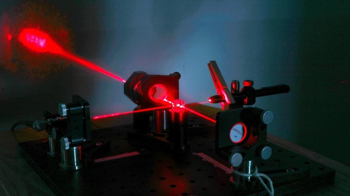 A tabletop model demonstrates how lasers are used in the 2 1/2 mile tunnels at LIGO. The laser beam on the right is split and sent to mirrors on the left and lower right to bounce back to the center. Because the mirrors are not at exactly the same distance, the light spot appears on the wall.