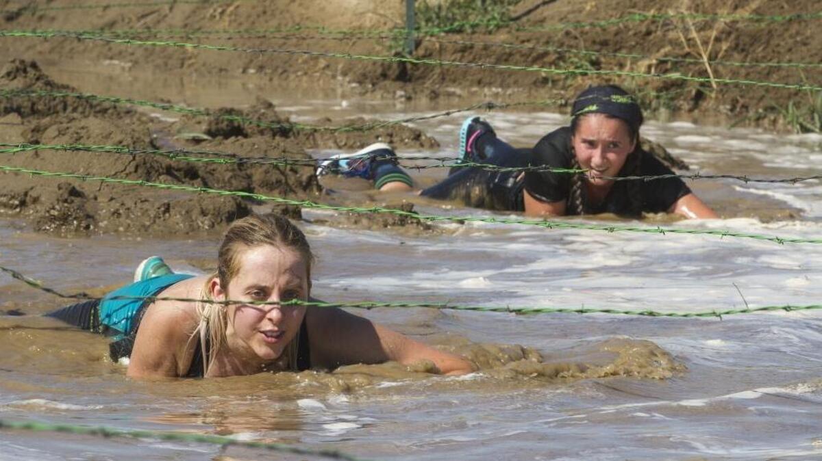 Margaret Pieczkowski, left and Alyssa Webb crawl below wires into muddy waters during the Renegade Rage Obstacle Race on Saturday at Hanses Farms in Pasco.