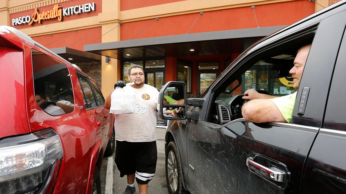 Coco Quintero, co-owner of Brothers Cheese Steaks, provides curbside delivery to customer Robert Bryson on Thursday outside the Pasco Specialty Kitchen. The Tri-City restaurant industry gained 400 jobs since last November.