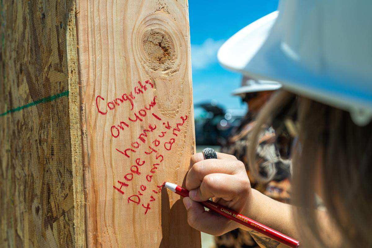 Volunteers write messages on the first wall of the future home of Avonlea and Buck Ide. The Ide family was selected to receive the First Story home at River North, a Haden Homes community being constructed in Benton City. First Story allows gives homebuyers a new, move-in ready home with zero-down and a zero-interest mortgage.