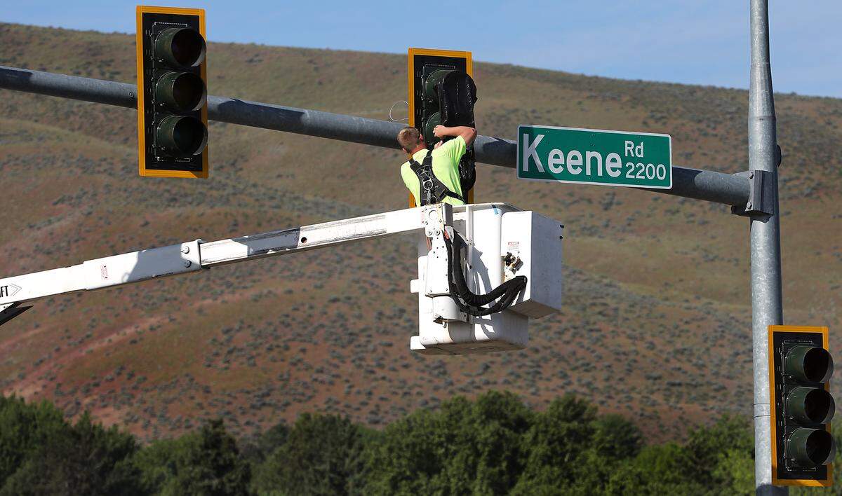 A workers removes the plastic covers on the traffic signals Wednesday morning for the opening the Queensgate Drive extension at Keene Road in south Richland.