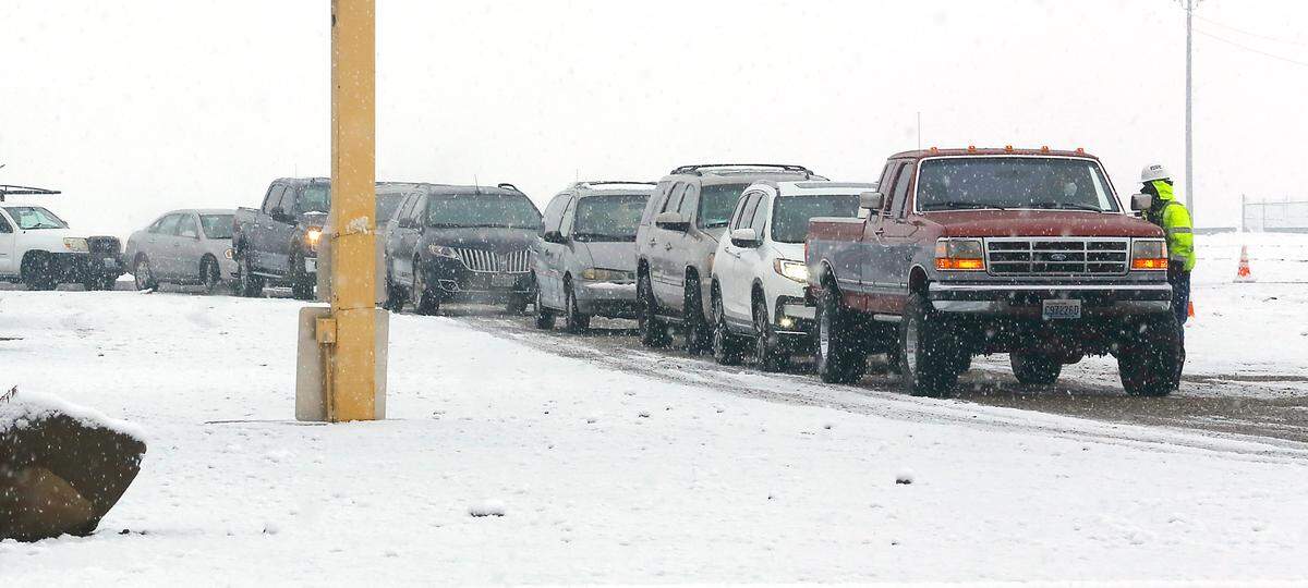 A volunteer checks vehicles into the snowy parking lot of Benton County Fairgrounds on the opening morning of the drive-thru mass COVID-19 vaccination site in Kennewick.