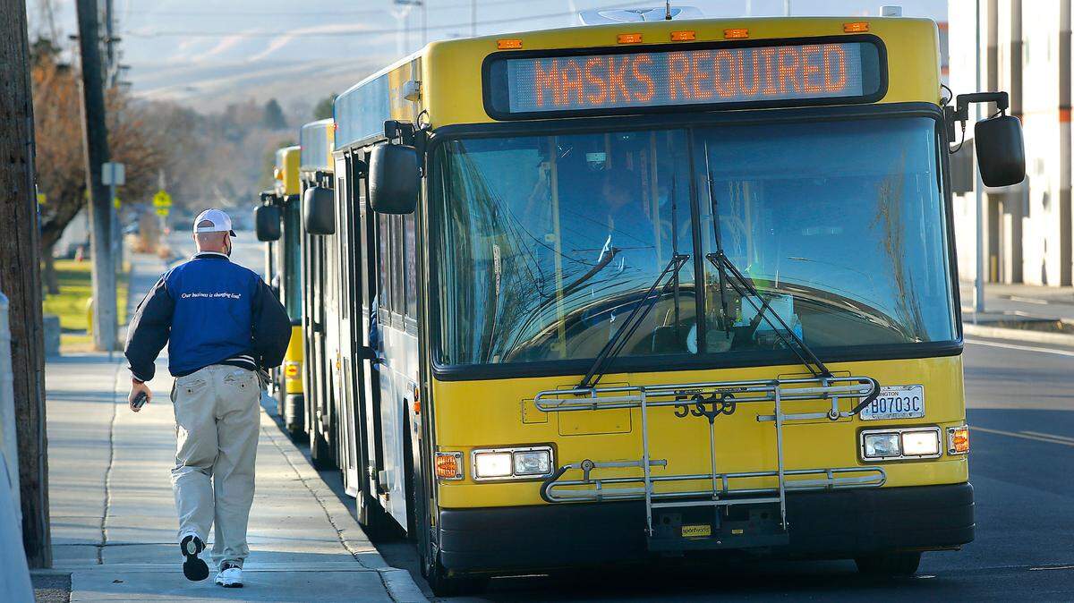 A Ben Franklin Transit rider boards a bus at the Dayton Street transfer station with a sign reminding customers they must wear masks during the ongoing coronavirus pandemic.