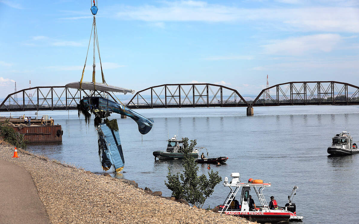 A crane on the Pasco shoreline lifts a floatplane that hit a power line across the Columbia River on Wednesday near the cable bridge. Officials say two men on the aircraft died in the crash.