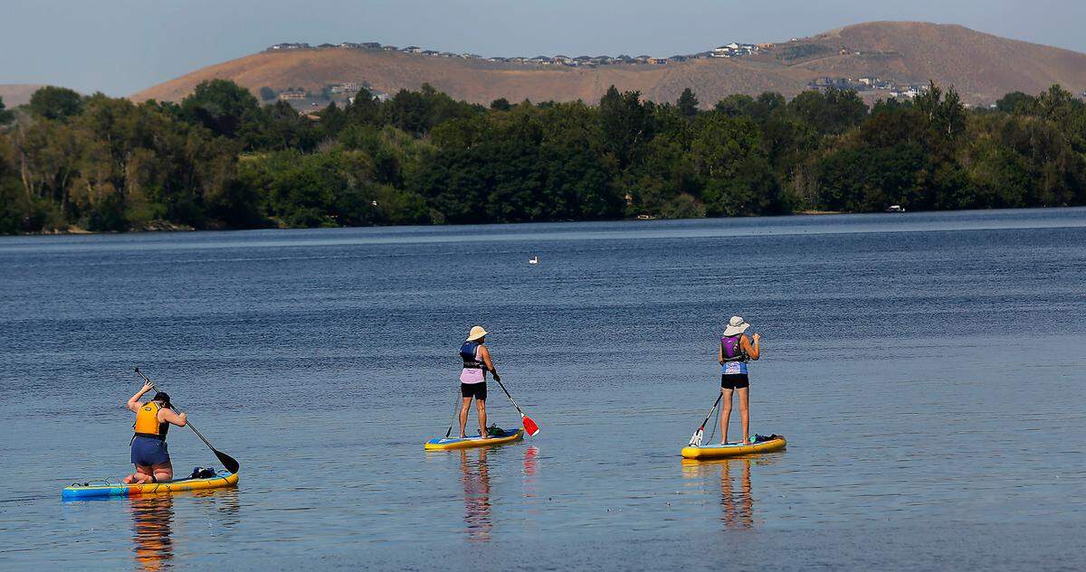 A trio of paddle board enthusiasts head upriver on a recent sunny summer morning from the Road 54 parking area for Wade Park along the Pasco shoreline of the Columbia River.