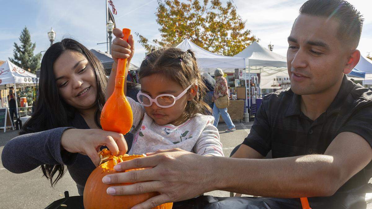 Parents Marissa Rios, left, Javier Gamez help their 3-year-old daughter, Mia Gamez, work on a Halloween masterpiece during a pumpkin carving party at the Historic Downtown Kennewick Farmers Market on Thursday. Hermiston Melon Company donated 60 pumpkins for the event.