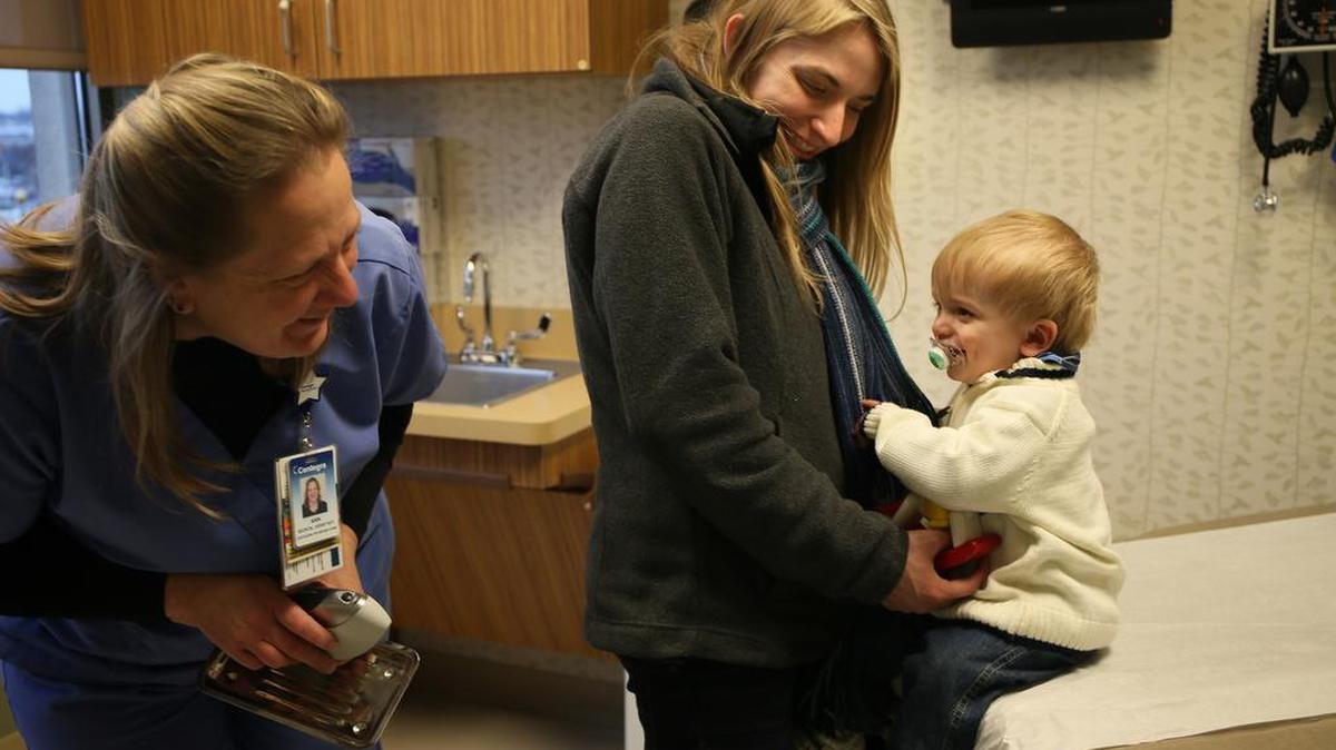 Landon Kuester, 13 months, plays peek-a-boo with nurse Ann Brown, left, at Centegra Physician Care-Crystal Lake on Dec. 3 in Crystal Lake, Ill. Holding Landon is his mom, Katie Frailey. Centegra Physician Care only treats children who are vaccinated, according to the Center for Disease Control and Prevention.