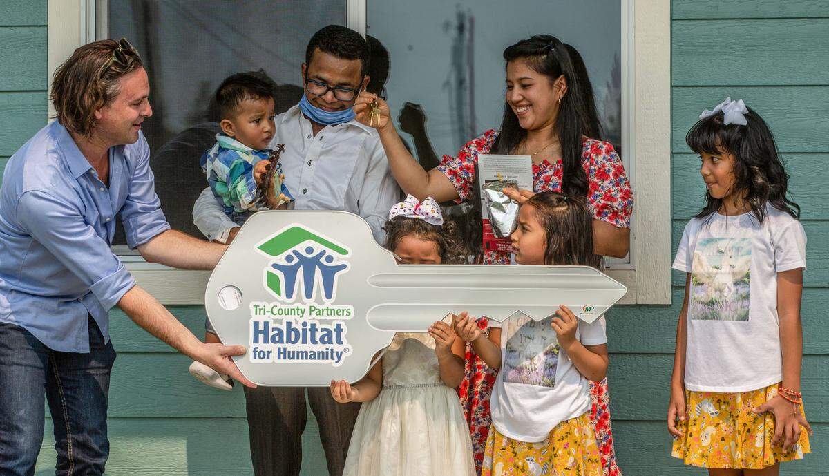 Jet Richardson, executive director at Habitat for Humanity Tri-County Partners, presents a giant key to Bawi Lian, Ruth Pretty and their children outside their new home in Pasco in 2021.