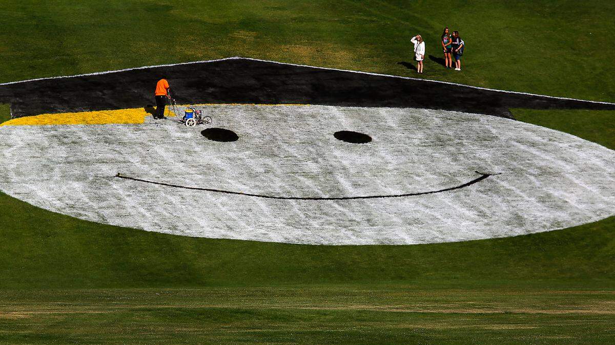 Carmichael Middle School students gather before class to watch as a Richland School District employee paints a larger-than-life graduation emoji on the hillside of the school on Thayer Drive. The creative display is best viewed from the Wellsian Way area.