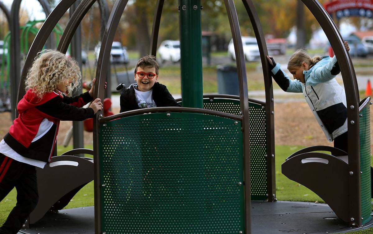 Kason Creed is all smiles as his friends push him around on the We-Go-Round at an inclusive playground area in Kennewick in 2023.