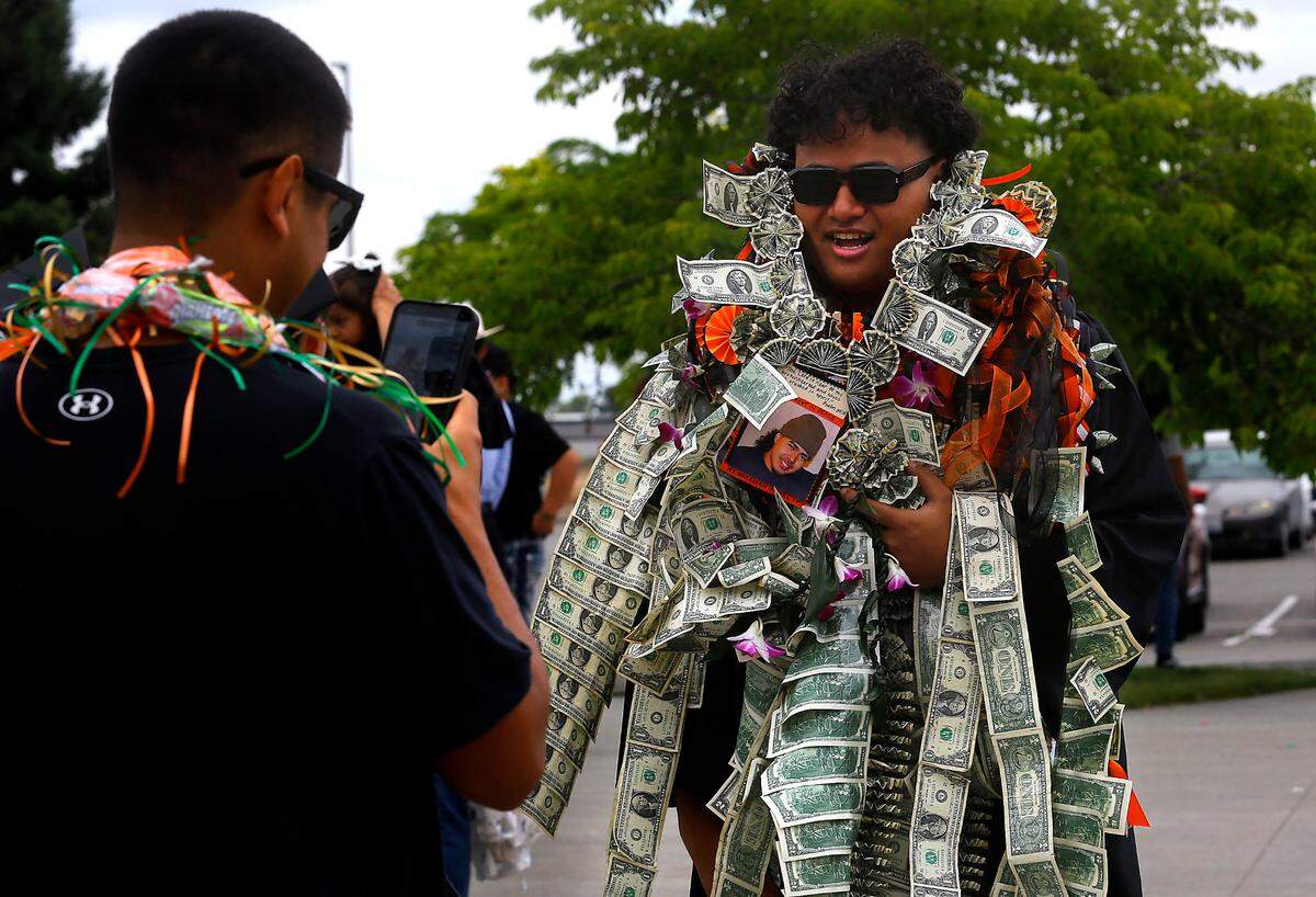 Kennewick High graduate Vea Moala poses for a photo with a family gift, wrapped around him, paper money taped together, following his 2023 graduation ceremony at the Toyota Center in Kennewick.