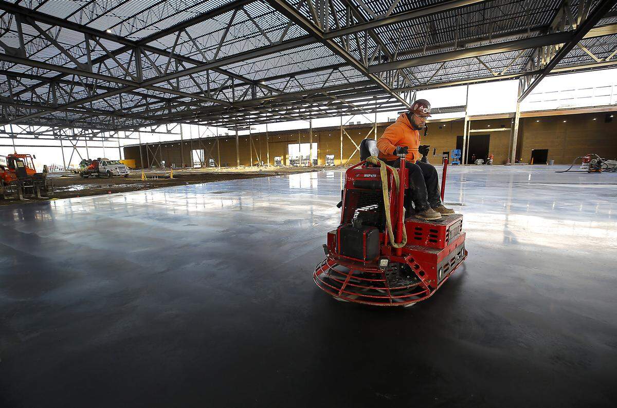 A construction worker polishes a freshly poured concrete floor in the open hall space of the Three Rivers Convention Center expansion in Kennewick.