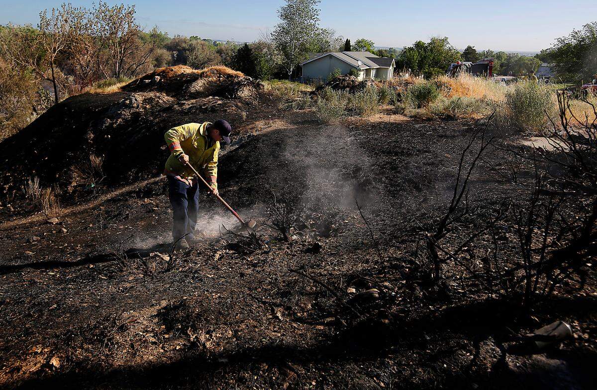 A Kennewick firefigher uses a shovel to extinguish a smoldering hot spot early Monday morning on the eastern edge of Zintel Canyon near South 8th Place.