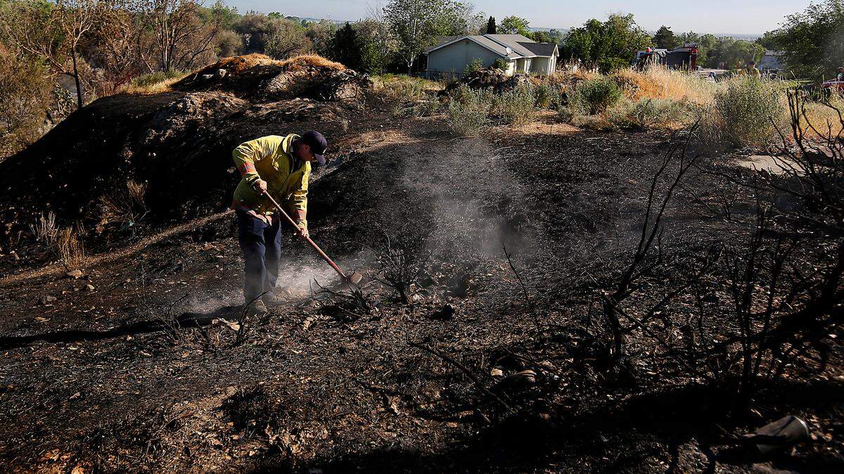A Kennewick firefigher uses a shovel to extinguish a smoldering hot spot after a fire raged on the eastern edge of Zintel Canyon.