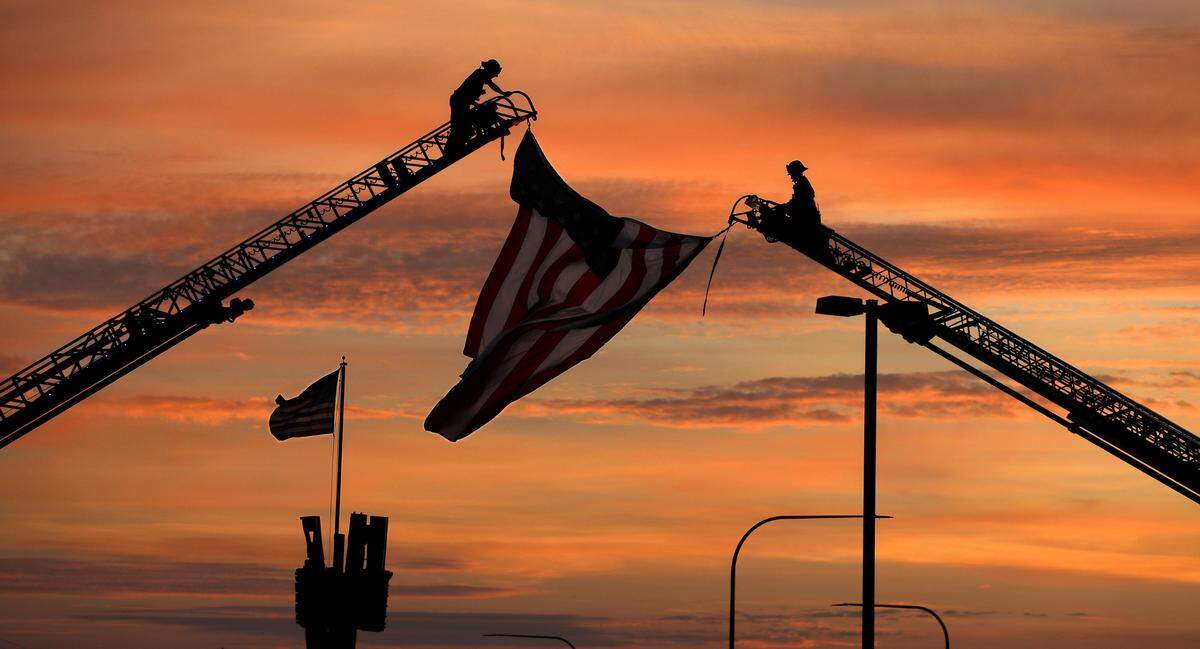Firefighters hang a large U.S. Flag from a Benton County Fire District 1 and Kennewick Fire Department aerial trucks at the 9/11 monument in Kennewick, WA.