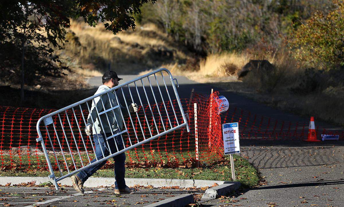 A Richland city employee carries a steel barricade to reinforce the temporary plastic fencing placed in late October to block the pathway in Columbia Park West.