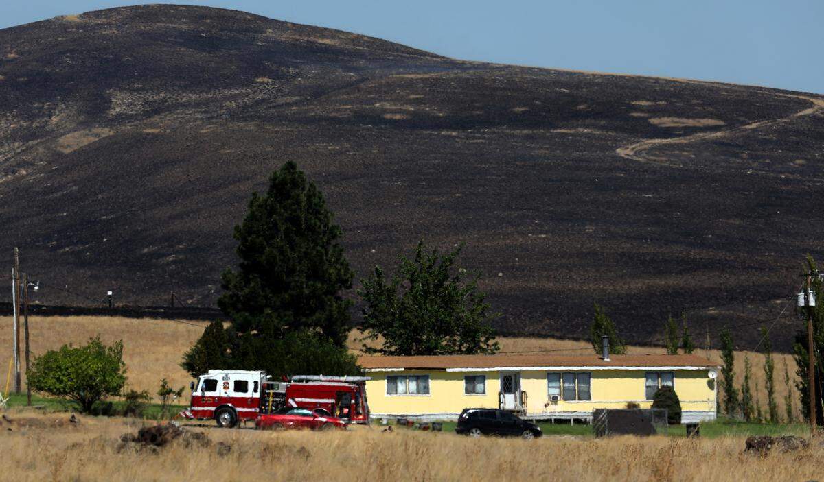 A fire truck stages next to a home that was threatened by a two-alarm wildfire Monday afternoon just north of Benton City. There were no immediate details on the size or cause of the blaze.