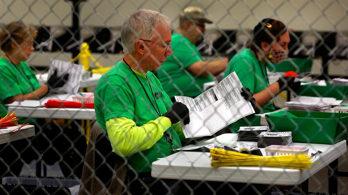 Benton County elections workers, seated in a chain link enclosure, open ballot envelopes in preparation for scanning and tabulating votes in 2022. A lawsuit claimed the signatures of Latino voters were being rejected at a higher rate in 2020.