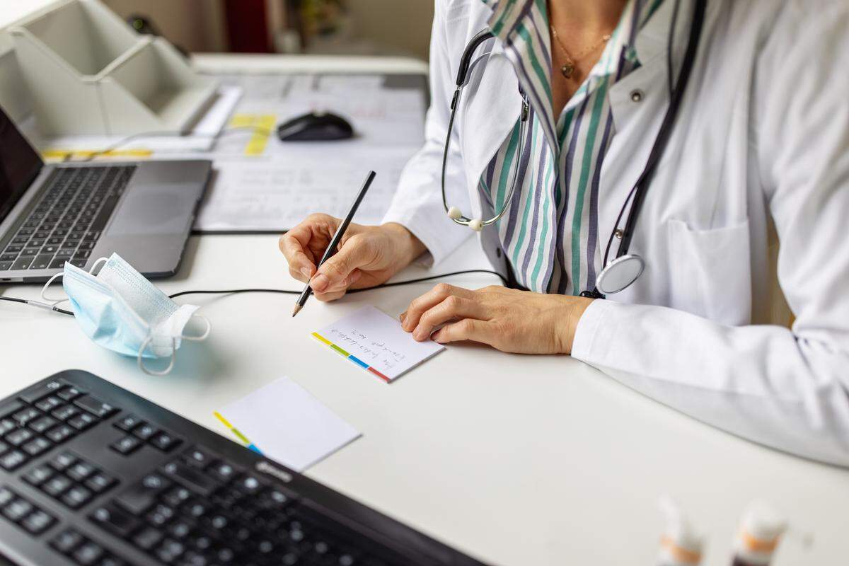 Close-up of a doctor preparing prescription while consulting a patient over video conference.