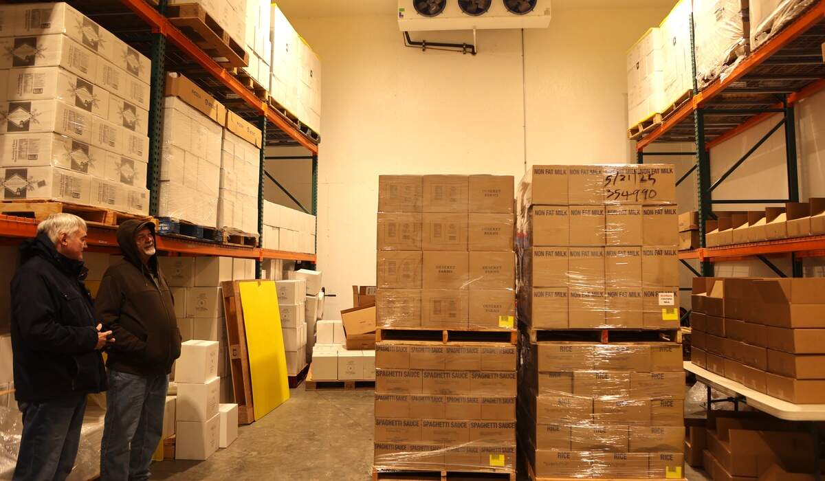 Tom Blodgett and Nolan Empey stand next to donated pallets of food inside a storage space at Empey Brothers Farms in Mesa.