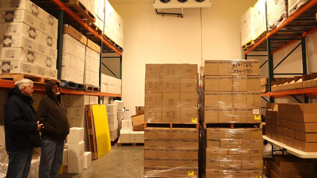 Tom Blodgett and Nolan Empey stand next to donated pallets of food inside a storage space at Empey Brothers Farms in Mesa.