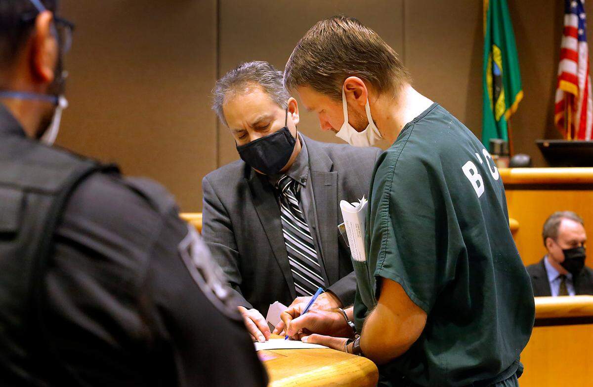 Aaron C. Kelly, 39, signs court papers, with guidance from bailiff Brian Ruegsegger, after making his first appearance Tuesday in Benton County Superior Court on charges he killed one and wounded another Monday inside the Richland Fred Meyer store.