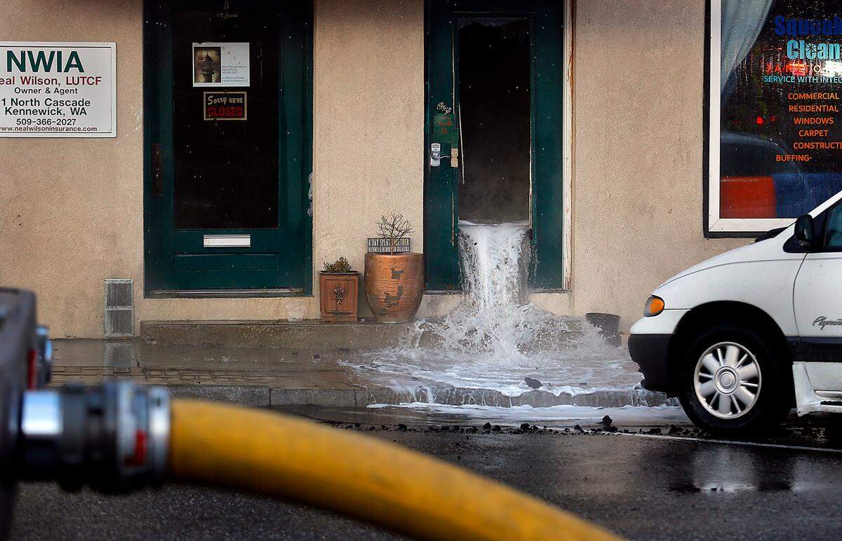 Water gushes out of a doorway from the stairs leading to second floor apartments during Friday’s early morning blaze at an historic two-story building on the corner of Cascade Street and Kennewick Avenue in downtown Kennewick.