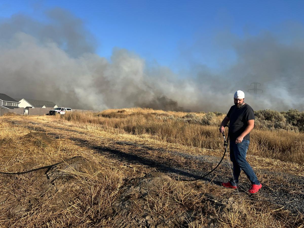 Matt Hagner sprays down brush behind his house in the 5700 block of West 41st Avenue as a fire threatens structures near Southridge High School in Kennewick.