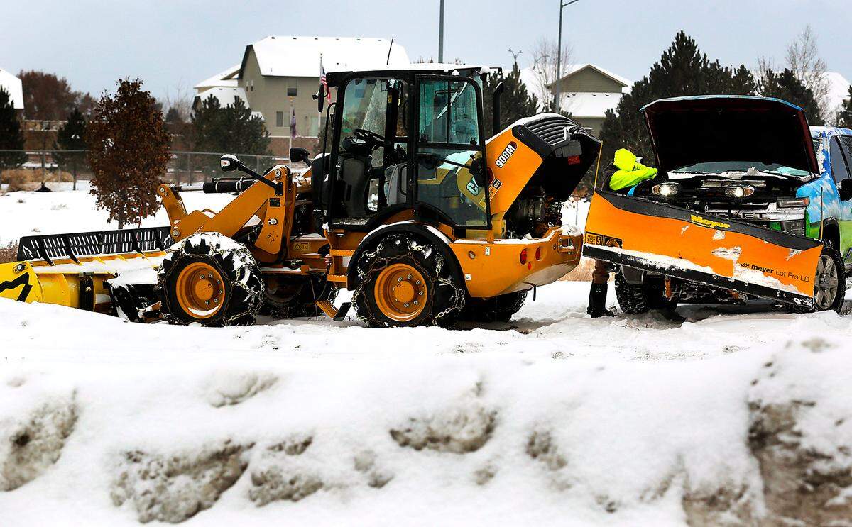 An employee of Galaxy Landscaping of Pasco uses a set of jumper cables and a work pickup to jump start a front end loader outfitted with a wide plow attachment early Friday at Trios Southridge Hospital in Kennewick.