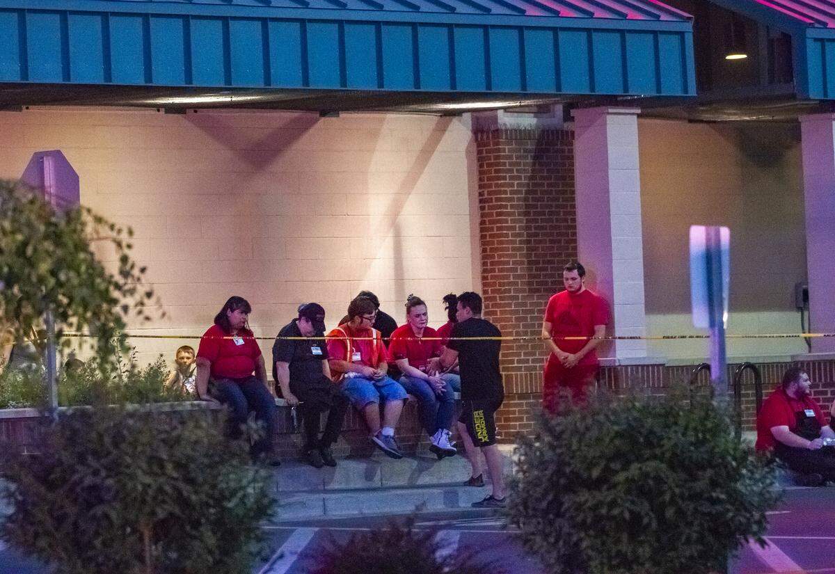 Winco employees and other shoppers sit outside and wait to be released by the police after a man shot a woman inside a WinCo store in Richland.