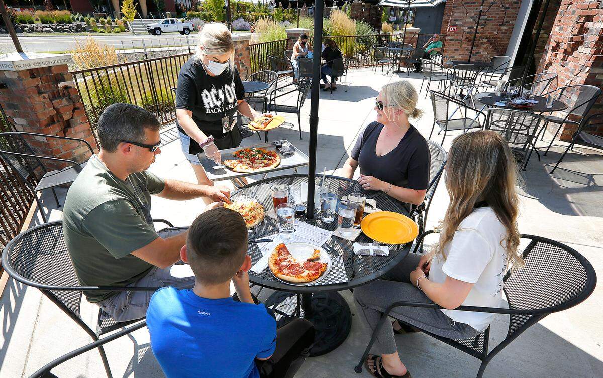 Server Serena Albertin dishes out pizza for customers outside on the patio of The Rock Wood Fired Pizza restaurant in south Kennewick.