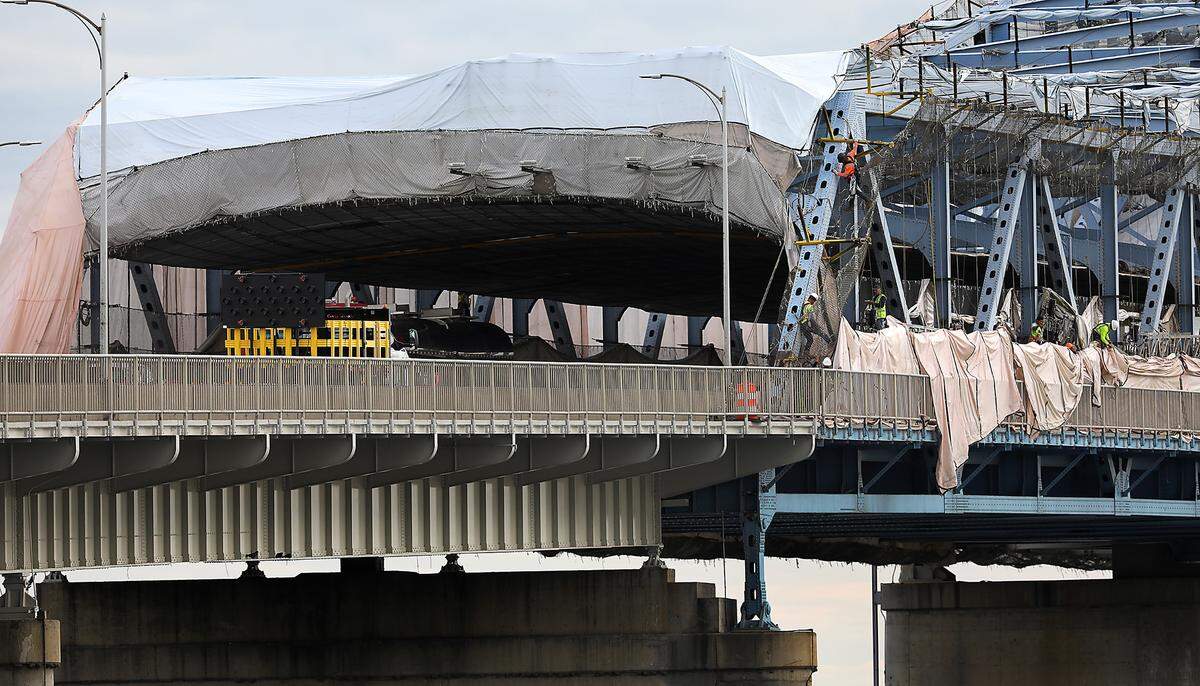 Construction workers climb on the girders Tuesday morning temporarily taking down the “cocoon” of tarps on the south side of the span.
