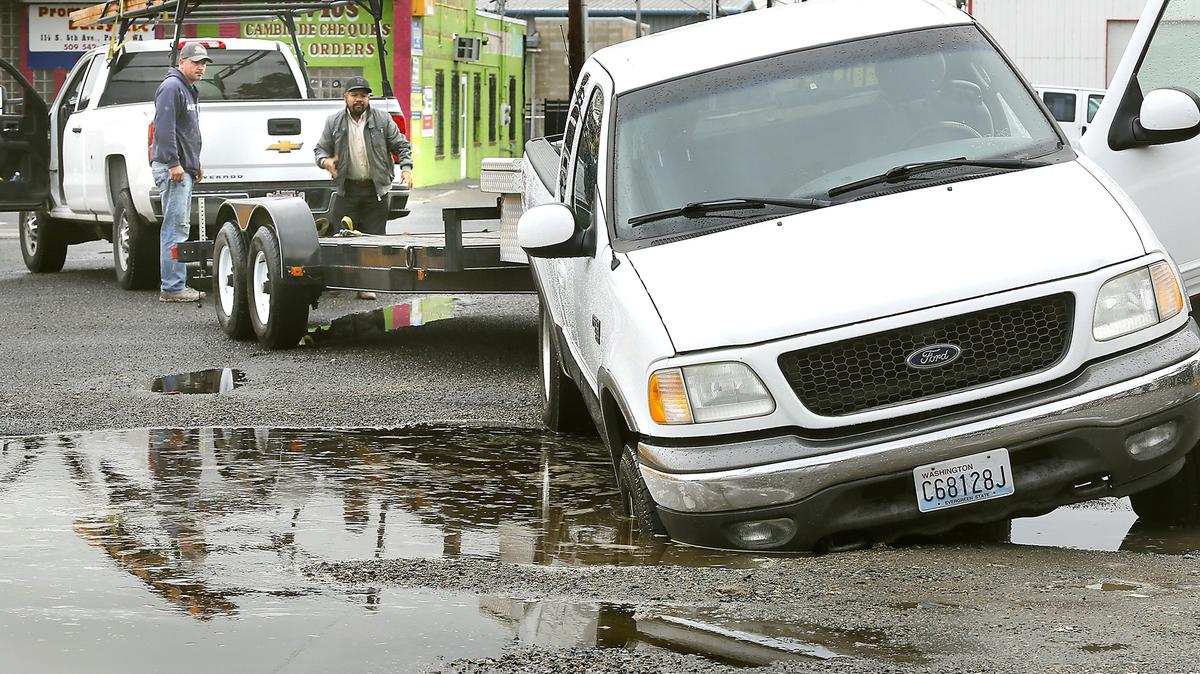 Good Samaritan Kenneth Stenersen of Richland, left, tries to help Auro Ramirez figure out how to free his truck and trailer Tuesday from a deep hole hidden under a rain puddle in the alley off South 5th Avenue between West Lewis and Columbia streets in Pasco.