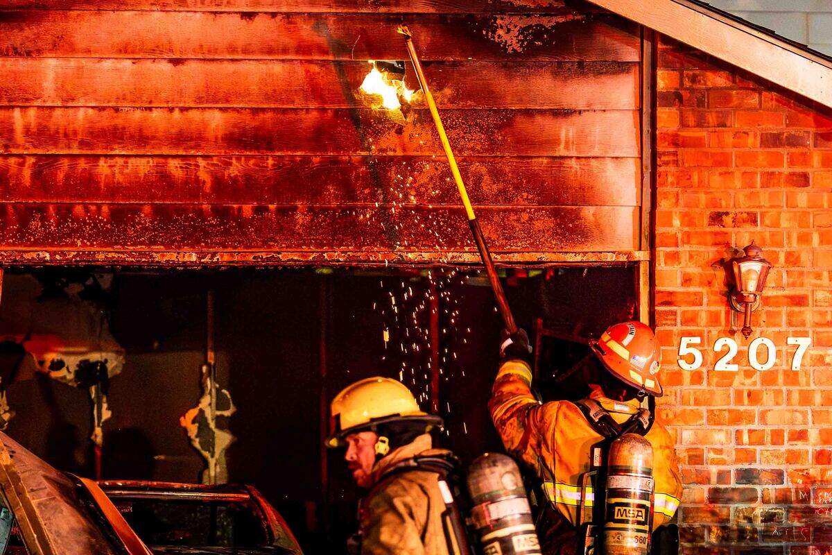 A firefighter uses a pike pole to expose hidden fire in the exterior wall of a garage during an early morning residential fire in the 5200 block of Jacksnipe Court.