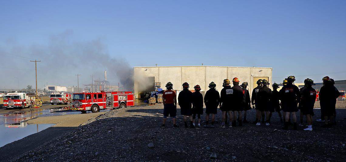 Fire recruits from the nearby training center observe from a distance as firefighters work on a fire at the Port of Pasco's Big Pasco Industrial Center.