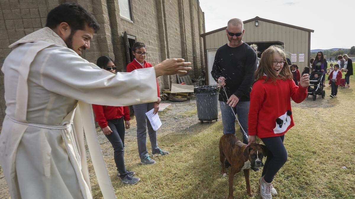 The Rev. Tomás Vazquez Tellez blesses a Boxer, Rhonda, and her owners Patrick Lyman and his daughter, Payton Lyman, 9, Thursday on the field outside of St. Joseph’s Catholic School in Kennewick for Feast Day for St. Frances of Assisi.