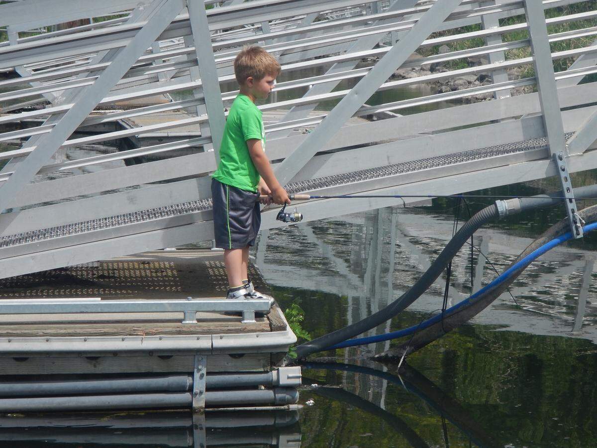 An aspiring young angler drops a line beside a local boat dock hoping to entice a smallmouth bass hiding in the shadows.
