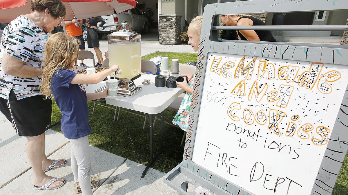 Sloane Stricker, 6, left, and Kennedy Stewart, 7, pour a glass of lemonade for Janet Wraspir of Kennewick on Sunday just moments after they opened their stand to show support for the firefighters who fought the fire in South Kennewick. The girls and their parents live in the Canyon Lakes area many homes were threatened. Watch video at: tricityherald.com/video