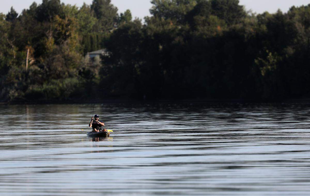 A barefoot kayak angler reels in his line while paddling around on the Columbia River early Thursday near Bateman Island in Richland. 