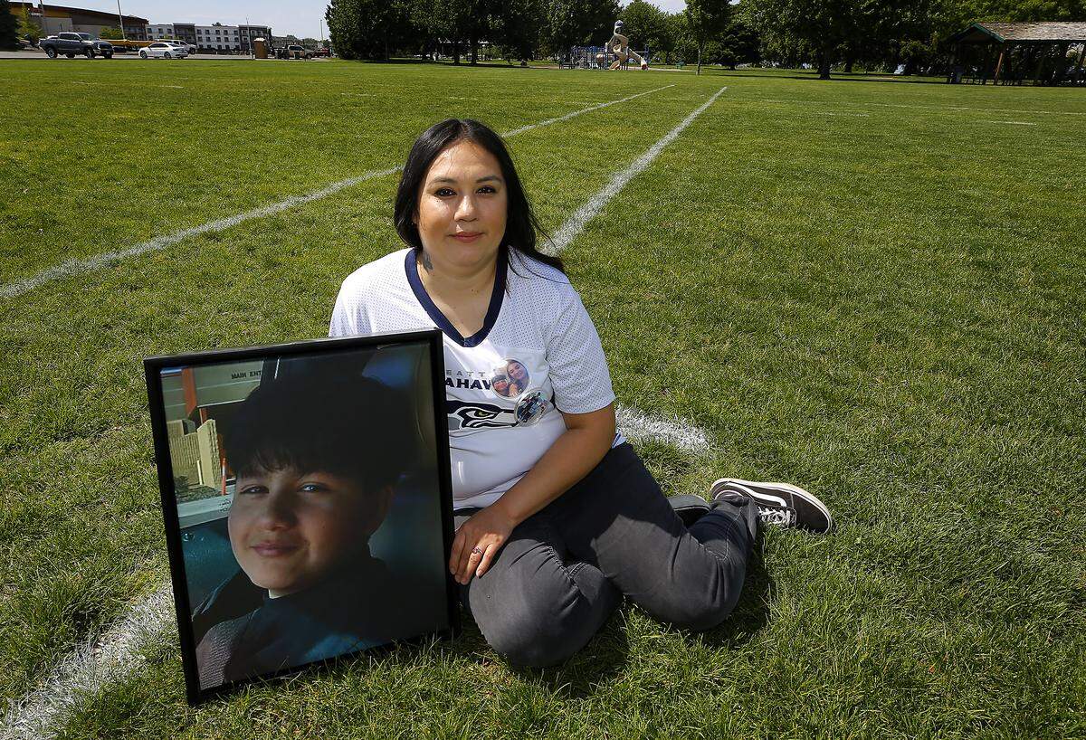 Sandra Ramirez holds portrait of her son, Joseph Martinez while wearing his flag football jersey on the fields he used to play on at the Columbia Point Marina Park in Richland. The 13-year-old was killed in a Kennewick shooting more than two years ago. 