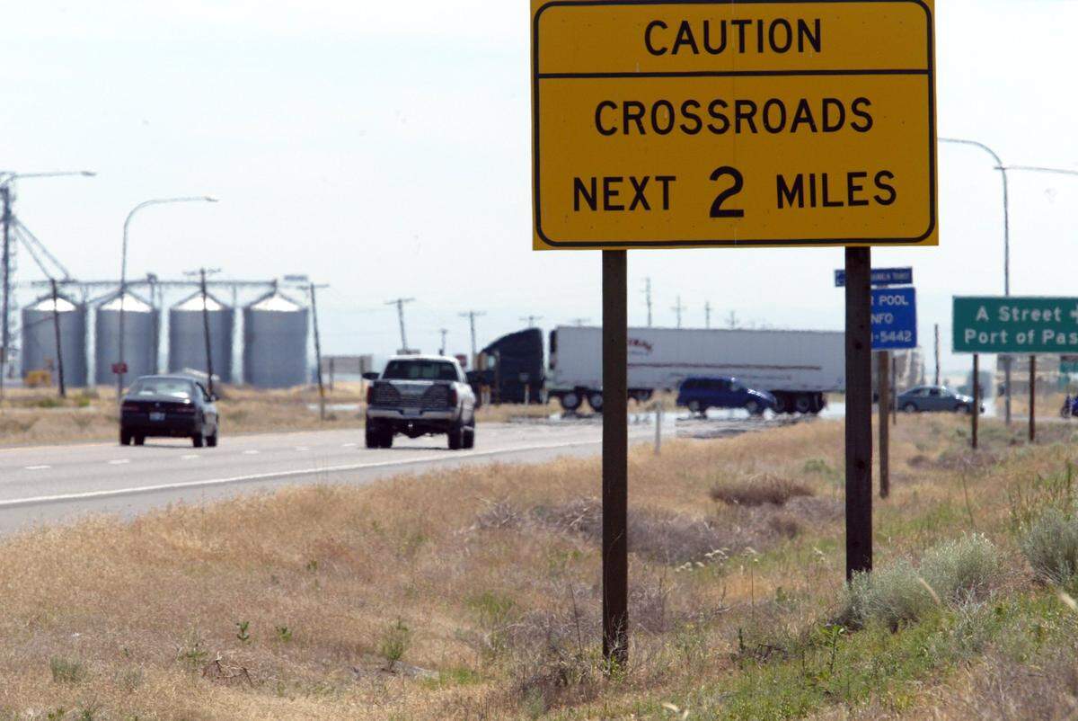 Passenger vehicles and a semi-truck cross Highway 12 at A Street in Pasco in front of eastbound traffic and just beyond a sign warning motorists of the intersections across the busy highway before the turn lanes at the intersection were modified by the Washington State Department of Transportation in 2021.