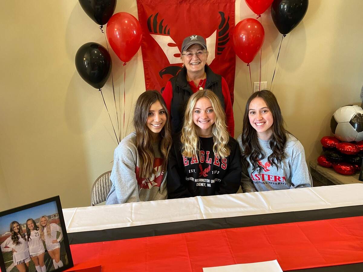 Kamiakin girls soccer coach Chris Erikson stands behind her three senior defenders — Claire Eerkes, Candace Carlson and Rylee Siefken — after the trio signed last fall to play for Eastern Washington University.