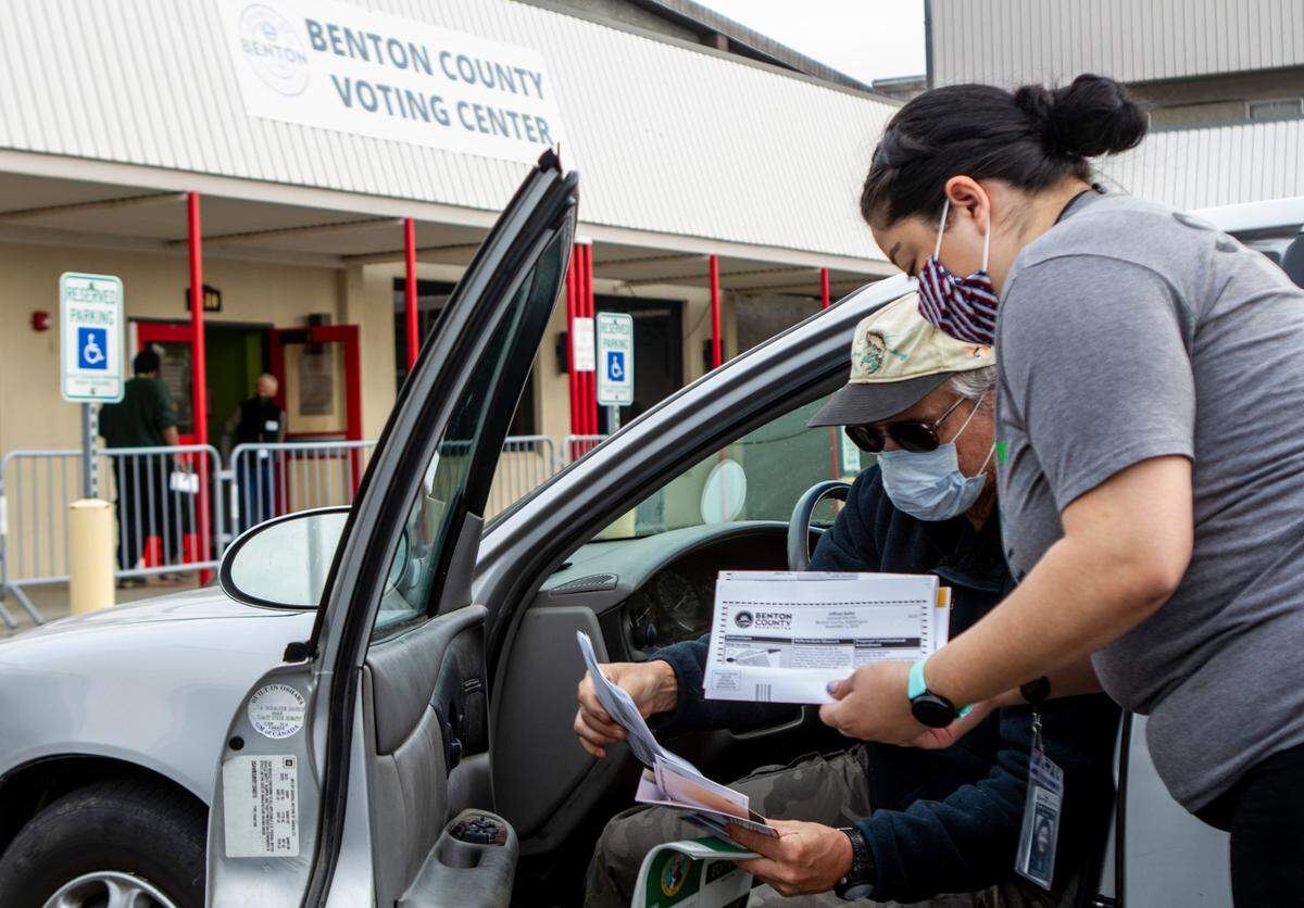 Brian Shultz, 59, looks over a ballot with auditor’s office employee, Miranda Cervantes, outside of the Benton County Voting Center in Richland, Wa. on Election Day. This year, due to the ongoing coronavirus pandemic, voters in Benton County could wait to be assisted by voting center staff in designated spots outside of the polling place.