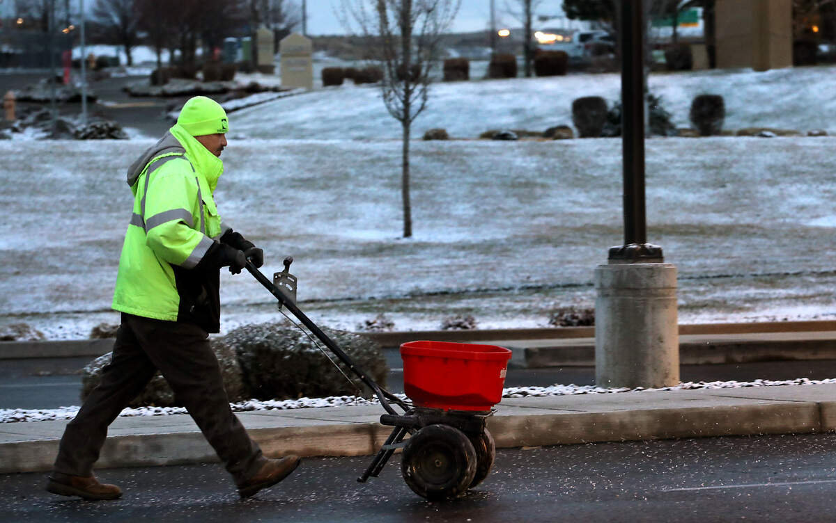 Heritage Landscape and Maintenance employee Julian Castellenos spreads ice melt granules on the sidewalk and parking lot of the STCU Southridge branch in Kennewick following an overnight dusting of snow in the Tri-Cities.