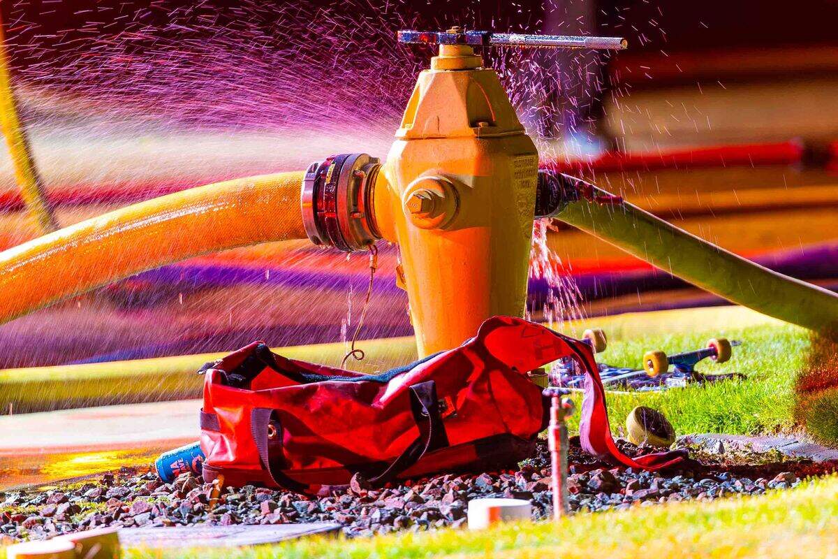 Water sprays from a fire hydrant supplying hose lines as firefighters battle an early morning residential fire.