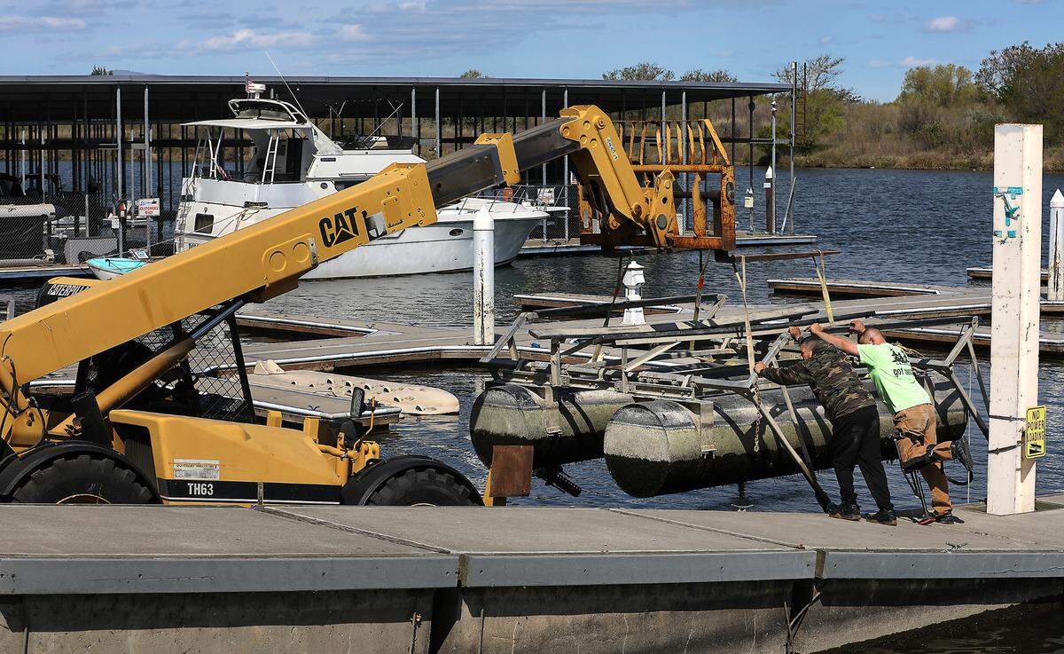 Workers prevent a boat lift from swinging on the straps connected to a boom lift while dismantling the Columbia Park Marina facility in Richland.