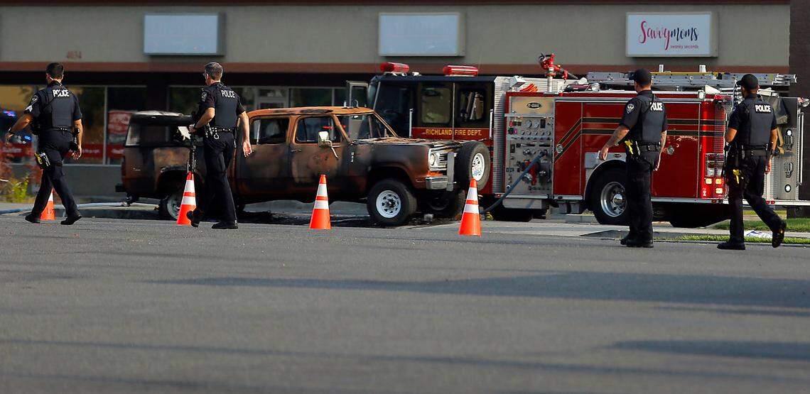 A line of police officers walk past the burned up pickup truck Wednesday near The Wash Stop car wash at 4024 W. Van Giesen St. in West Richland. The driver was involved in shootings and arson fires starting in Finley.