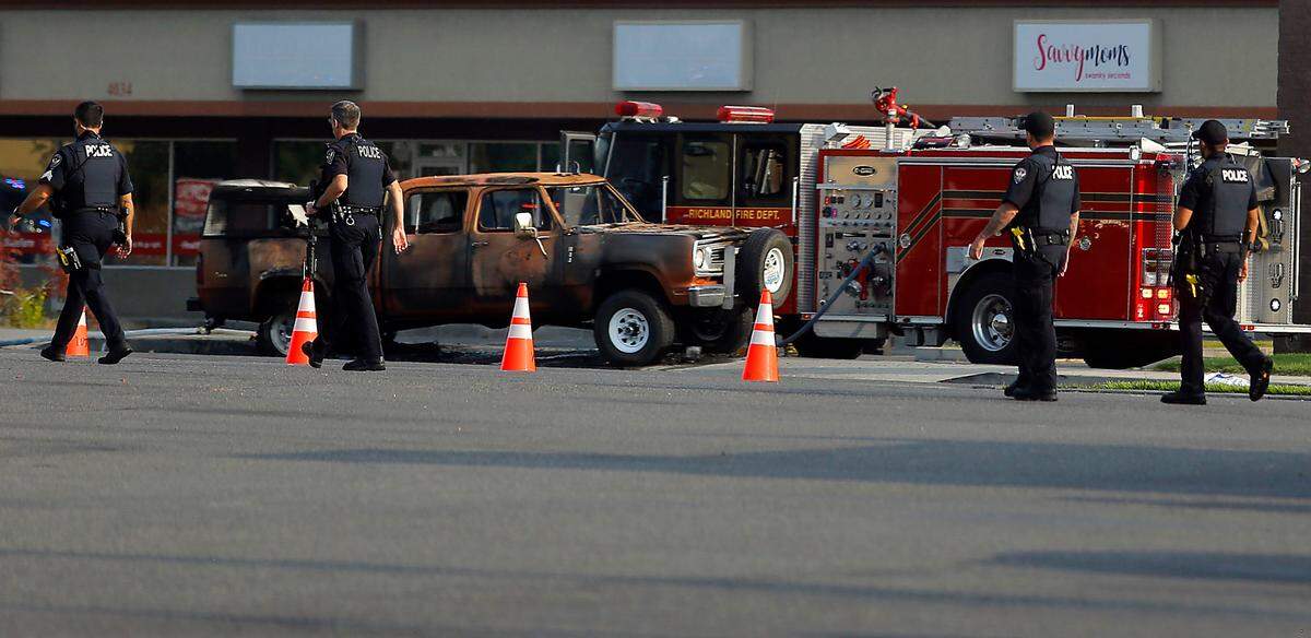 A line of police officers walk past the burned up pickup truck Aug. 25, 2021, in West Richland. The driver, Ryan Kaufman, died inside the truck after the pickup caught fire and there was a gunfire exchange with police.