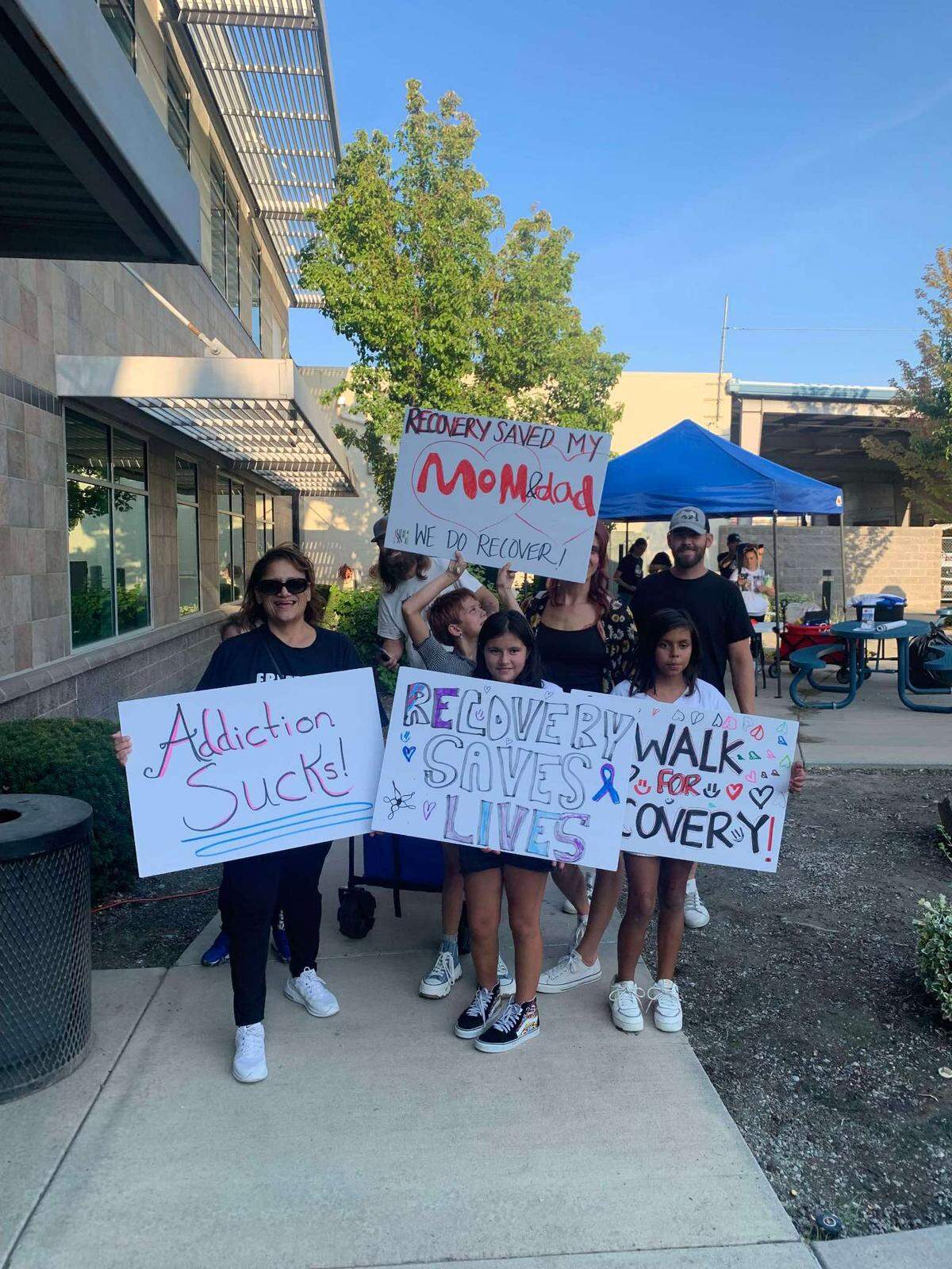 A family holds signs with messages about addition and overdose awareness during the 2023 Hands Across the Bridge Tri-Cities event.